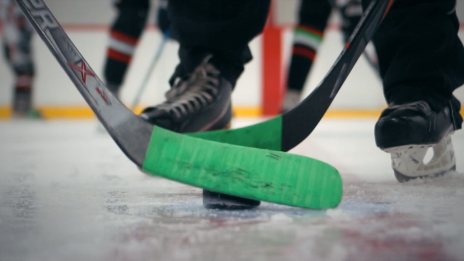 Two green-taped sticks meeting on the puck at face-off